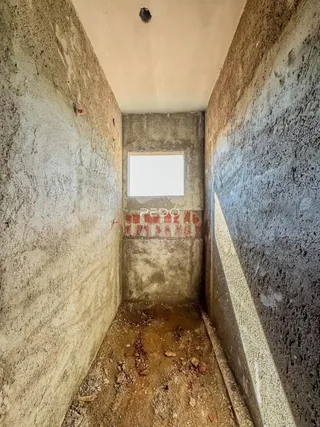 A imagem mostra um corredor estreito com paredes de alvenaria e piso de terra.