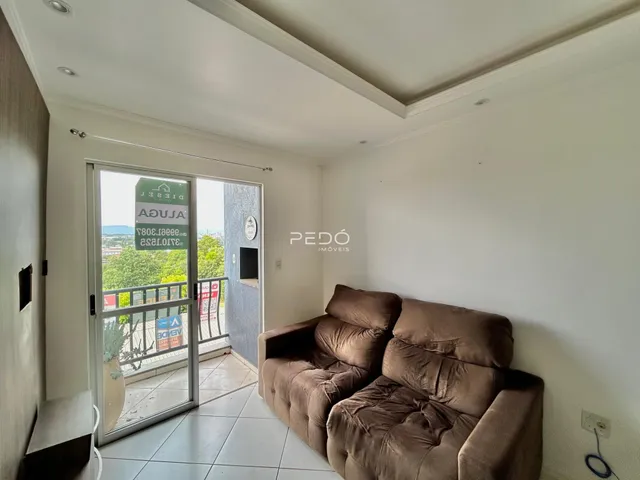 Sala de estar com sofá marrom e porta de vidro dando acesso à varanda.