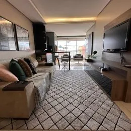 Foto interna de uma sala de estar com sofá e televisão montada na parede.