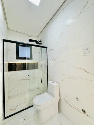 Banheiro com revestimento em mármore branco e box de vidro.