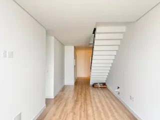 Hall de entrada com piso de madeira clara e escadaria branca.