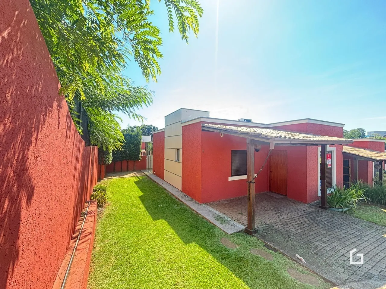 Vista externa de uma propriedade com jardim verde e parede vermelha.