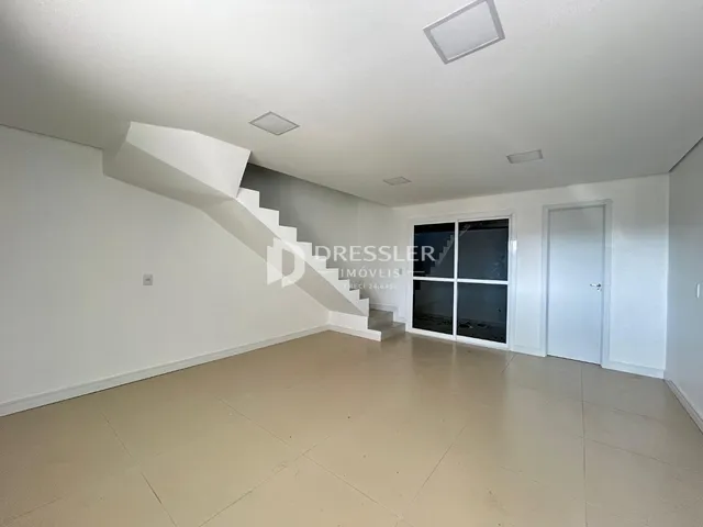 Uma sala de estar com piso claro e escadaria interna.