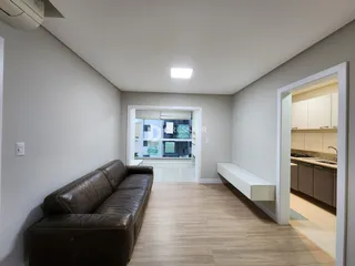 Sala de estar com sofá de couro marrom e piso de madeira clara.