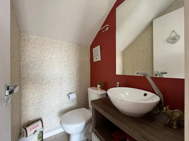 Foto interna de um banheiro com louças brancas e parede decorada em vermelho.