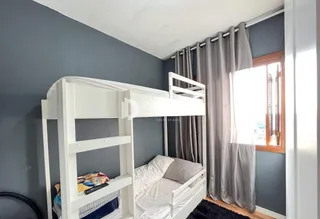 Quarto com cama de beliche branca e janela em ambiente com paredes cinzas.