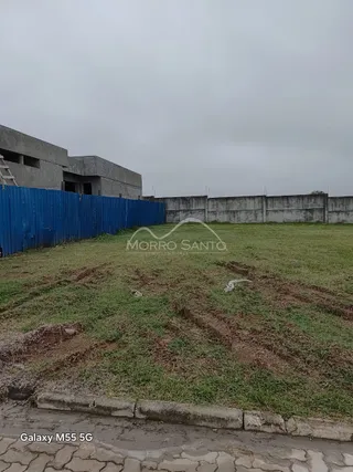 Vista externa de um terreno com grama seca e cerca azul.