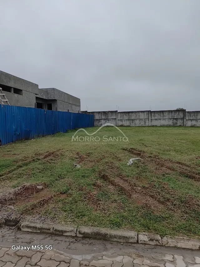 Vista externa de um terreno com grama seca e cerca azul.