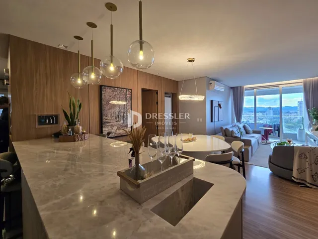 Interior de uma sala de estar com ilha de cozinha e vista para a paisagem.