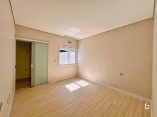 Ambiente interno de uma sala com piso de madeira clara e paredes bege.