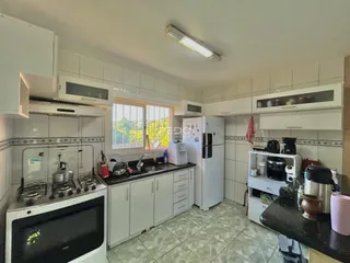 A cozinha apresenta armários brancos e piso claro.
