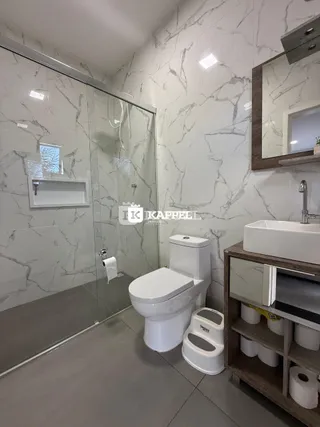 Banheiro com revestimento de mármore branco e piso cinza.