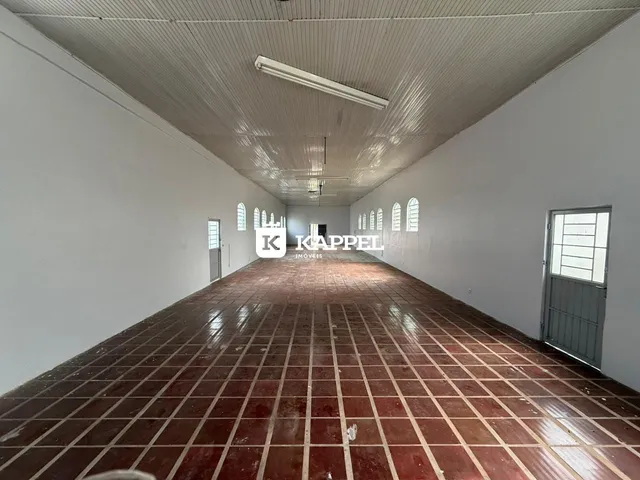 Corredor longo com piso de ladrilhos vermelhos e teto de painel branco.