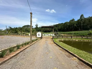 Vista externa de uma estrada de terra que leva a uma área com um corpo d'água e vegetação.