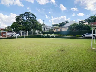 Vista de um grande gramado com cerca e residências ao fundo.