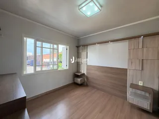 A sala apresenta piso de madeira e grandes janelas com vista externa.