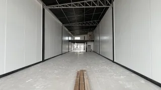 Corredor interno com paredes brancas e teto de estrutura metálica exposta.
