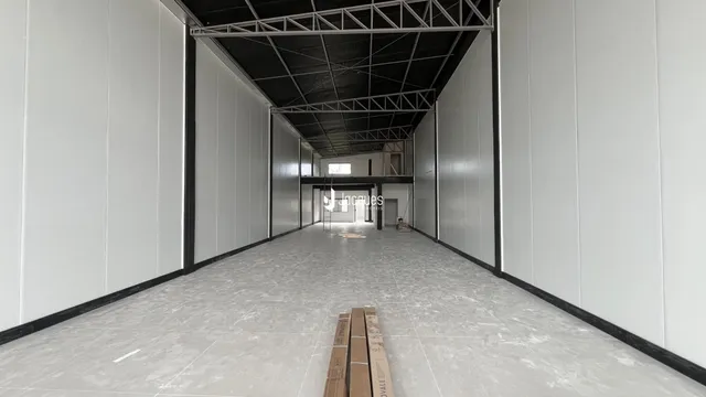 Corredor interno com paredes brancas e teto de estrutura metálica exposta.