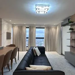 Sala de estar com sofá escuro e cortinas claras em um apartamento.