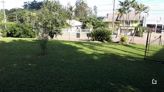 Vista externa de um terreno gramado com cercas e casas ao fundo.