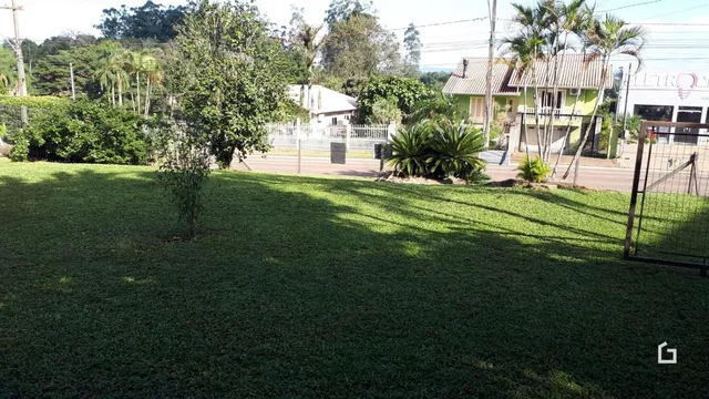 Vista externa de um terreno gramado com cercas e casas ao fundo.