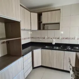 Foto interna de uma cozinha com armários brancos e bancadas escuras.