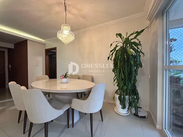 Uma sala de jantar clara com mesa redonda e cadeiras brancas.