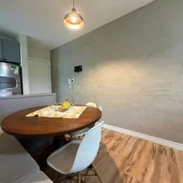 Mesa redonda de madeira com uma cadeira branca está visível na sala.