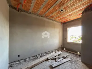 Interior da sala em construção com teto de madeira exposto e paredes em fase de acabamento.