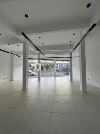 Vista interna de um espaço amplo com piso de cerâmica e vigas no teto.