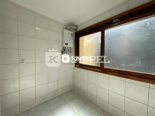 Vista interna de um corredor com paredes brancas e janela de madeira.