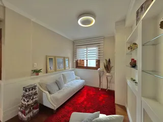 Sala de estar com sofá branco e tapete vermelho em um imóvel no Brasil.