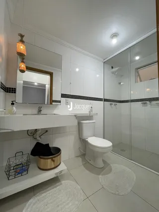 Banheiro com revestimento branco e box de vidro transparente.