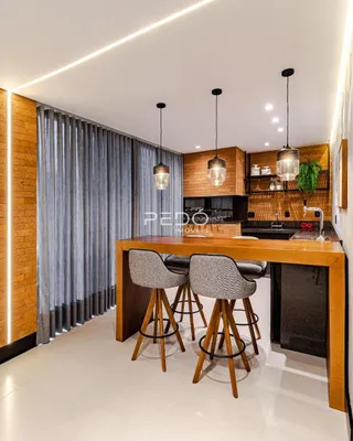 Ambiente moderno com ilha de madeira e luminárias pendentes em um espaço aberto.