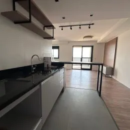 Foto interna de uma cozinha com armários escuros e bancadas escuras.