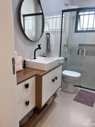 Banheiro com bancada de madeira e pia branca e vaso sanitário visível.