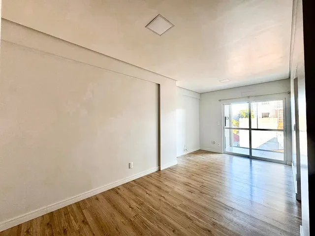Uma sala ampla com piso de madeira clara e porta de vidro que dá acesso ao exterior.