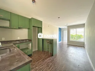 Interior de uma cozinha com armários verdes e piso de madeira clara.