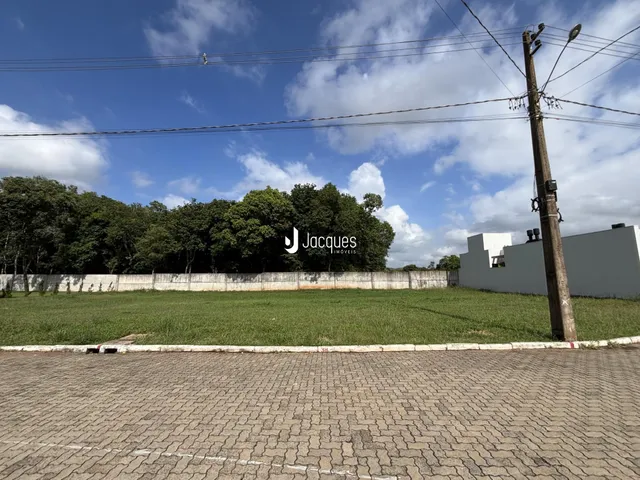 Vista externa de um terreno gramado com cerca e árvores ao fundo.