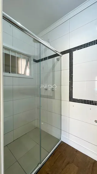 Vista interna de um banheiro com box de vidro e revestimento branco.