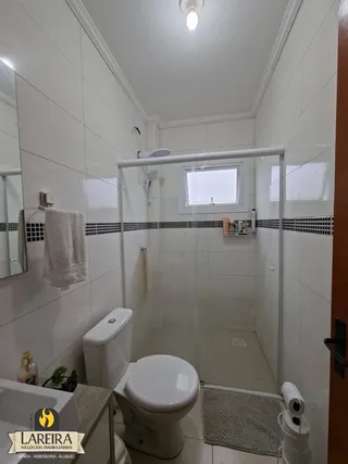 Banheiro com revestimento cerâmico e box de vidro.