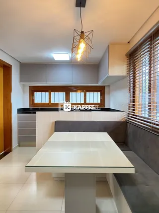 Sala de jantar moderna com mesa de vidro e bancada de cozinha em ambiente claro.