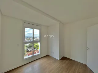 Ambiente interno de uma sala com piso de madeira clara e janela com vista para o exterior.
