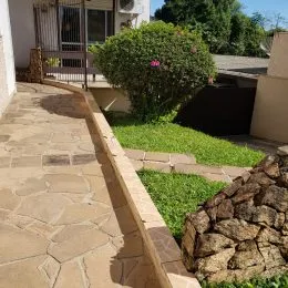 Caminho de pedra ao lado de um muro de contenção com vegetação em uma propriedade.