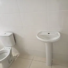 Foto de uma pia branca instalada em uma parede revestida de azulejos brancos.