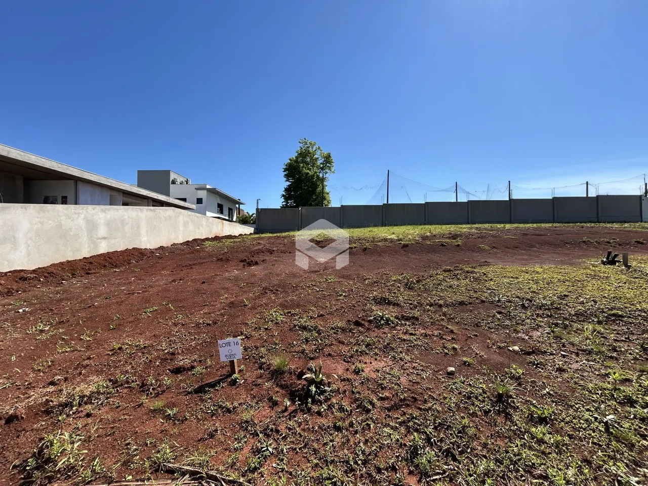 Vista de um terreno aberto com vegetação rasteira e uma cerca de fundo.