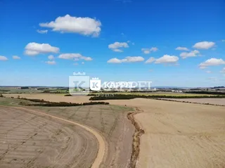 Vista de campos abertos e terra arada sob um céu azul com nuvens.
