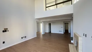 Ambiente interno amplo com piso de madeira clara e paredes brancas, com vista para um andar superior.