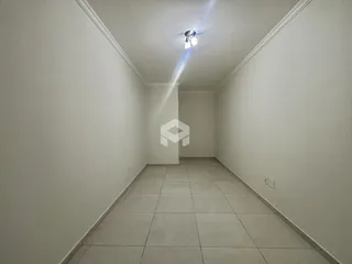 Um corredor longo com paredes brancas e piso de cerâmica claro.