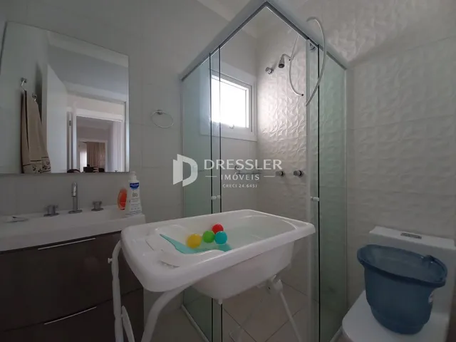 Interior de um banheiro com box de vidro e pia branca.